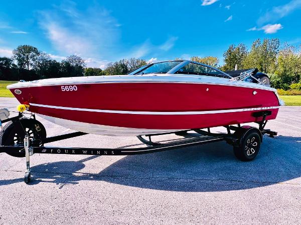 Slide: The Image of 2023 Four Winns H1 OB boat on a trailer, red hull, outdoors. - 1