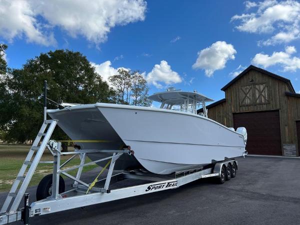 Slide: The Image of 2022 Freeman 37 VH boat on a Sport Trail trailer, parked near a wooden barn. - 0