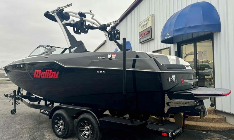 Slide: The Image of 2024 Malibu M220 boat on trailer outside dealership, black exterior, sleek design. - 23