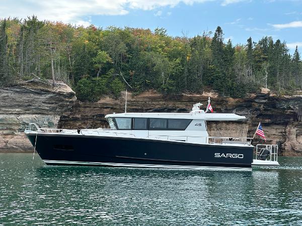 Slide: The Image of 2023 Sargo 45 boat cruising near rocky shoreline with lush greenery. - 1